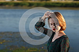 The girl in a green authentic dress walks at sunset on the coast of a reservoir