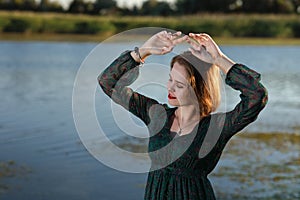 The girl in a green authentic dress walks at sunset on the coast of a reservoir