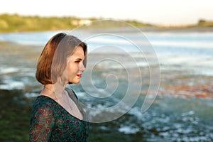 The girl in a green authentic dress walks at sunset on the coast of a reservoir