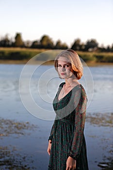 The girl in a green authentic dress walks at sunset on the coast of a reservoir