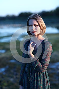 The girl in a green authentic dress walks at sunset on the coast of a reservoir