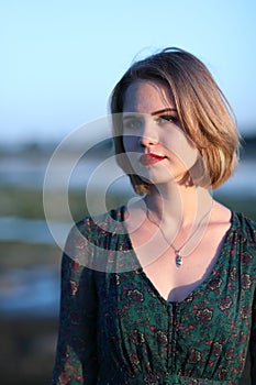 The girl in a green authentic dress walks at sunset on the coast of a reservoir