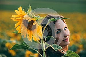 Girl in a green dress and long blond hair in a sunflower field, smiles and enjoys the moment. The concept of summer and sun.