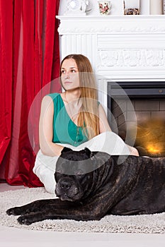 Girl in green dress sitting by the fireplace with dog Cane Corso