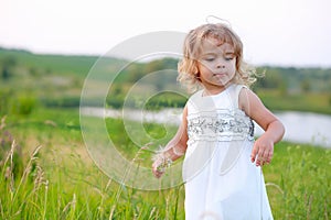 Girl in a green field with a big dandelion on the background of the lake