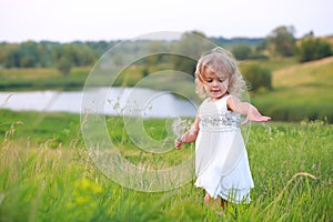 Girl in a green field with a big dandelion on the background of the lake