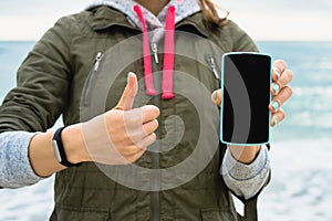 Girl in the green jacket on the beach showing the mobile phone s