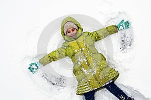 A girl in a green jacket plays in the snow in frosty weather. Above view of adorable little girl enjoying beautiful