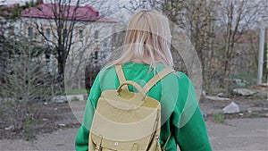 A girl in a green sweater with a backpack behind him is an abandoned wasteland in the city. The camera moves behind her.