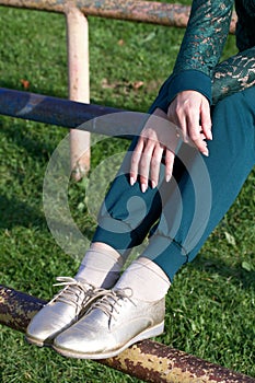 Girl in a green tracksuit and golden shoes. On a Sportsground. Close-up of the legs