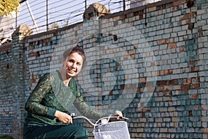 The girl in a green tracksuit. Standing, holding the handlebars of the bike. Against the background of a brick wall