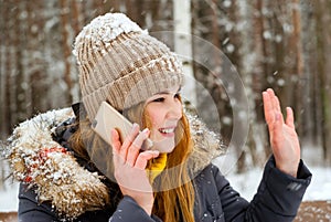 Girl greets someone by hand, talking on the phone in the winter in the open air