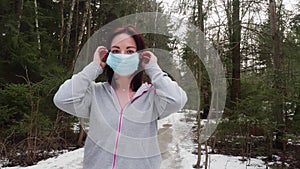 Girl in grey hoody puts on disposable medical mask and shows thumb up gesture