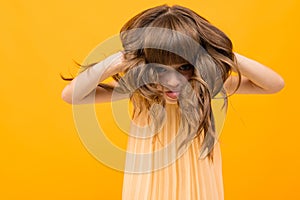 Girl grimaces and twists her hair on a yellow background