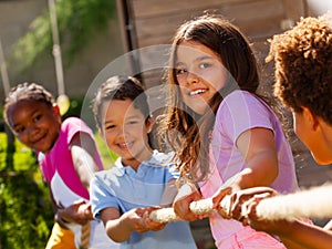 Girl in group of diverse kids pull rope play game