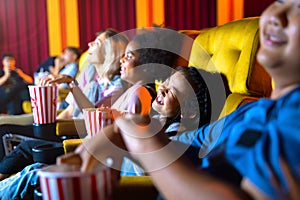 The girl and group of kid are seating and watching the cinema at movie theater seats. The faces have feeling happy and enjoy