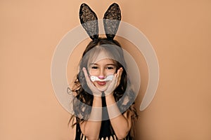 Girl in guise of an Easter bunny holds her cheeks with hands smiling sweetly