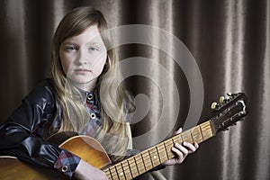 Girl with a guitar on a brown background. Child with a musical instrument
