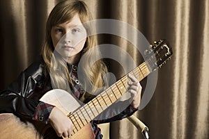 Girl with a guitar on a brown background. Child with a musical instrument