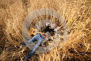 Girl with a guitar lying in the wheat field,