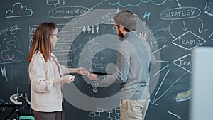 Girl and guy discussing business strategy and writing on chalkboard wall indoors