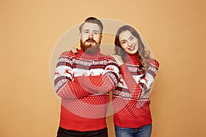 Girl and a guy dressed in red and white sweaters with deer stand together on a beige background in the studio
