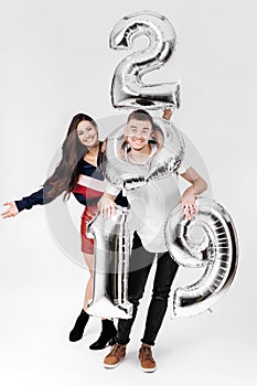 Girl and guy dressed in a stylish clothes are having fun with balloons in the shape of numbers 2019 on a white