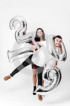 Girl and guy dressed in a stylish smart clothes are having fun with balloons in the shape of numbers 2019 on a white