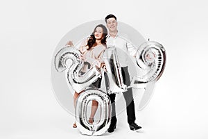 Girl and guy dressed in a stylish smart clothes are holding balloons in the shape of numbers 2019 on a white background