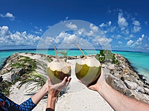 Girl and a guy holding fresh coconuts with a pipe in front of the ocean in the Maldives on a stone pier. Wide format
