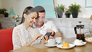 Girl and guy looks at mobile phone at table in sweet shop