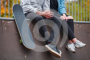 A girl with a guy sitting on the run-up next to a skateboard in a skate park