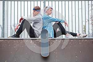 The girl with the guy sitting back to back looking in different directions on the dispersal in the skate park