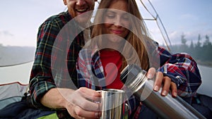 Girl and guy spending time together in tent. Smiling woman pouring tea into cup