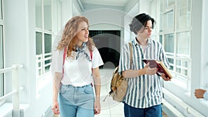 Girl and guy students walking in high school hall talking giving books to mates