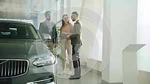 Girl and guy talking to salesman in car dealership choosing automobile together