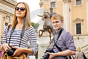 Girl and guy tourists with cameras in Rome at statue with rider