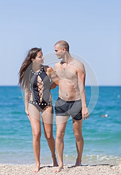 Girl and guy walk along sea looking each at other
