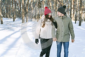 Girl and guy are walking in the winter park and look at each other. Young couple in snowy forest