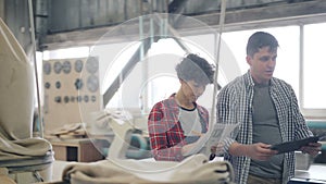 Girl and guy walking in wood workshop talking holding tablet and paper documents