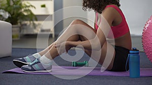 Girl in gym outfit sitting on floor and massaging cramped leg, strained muscle