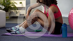 Girl in gym outfit sitting on floor and massaging cramped leg, strained muscle