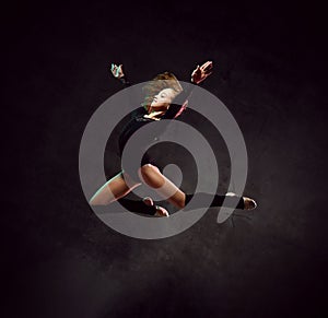 Girl gymnast in black sport body and uppers jumping and making dymnastic pose in air over dark background