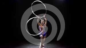 Girl gymnast twists the hoops and dances . Black background
