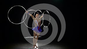 Girl gymnast twists a lot of metal hoops on her body. Black background. Slow motion