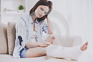 Girl With Gyps Sitting on Sofa and Looking at Leg.