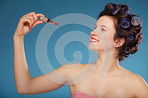 Girl in hair curlers applying red lipstick