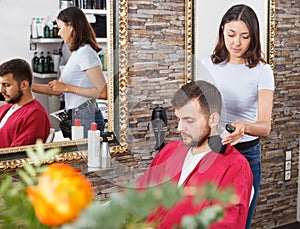 Girl hairdresser cuts hair of young man client at beauty salon