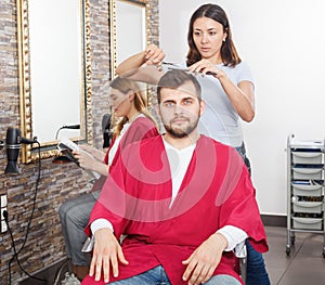 Girl hairdresser cuts hair of young man client at beauty salon