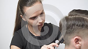 The girl hairdresser with the help of scissors and a comb cuts the hair on the back of the guy`s head.